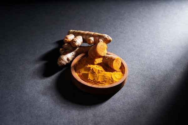 Turmeric roots and powder in a wooden bowl.